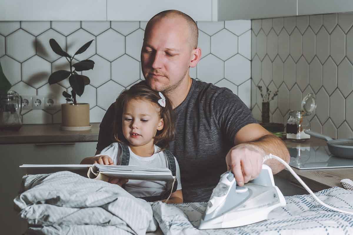 parent doing laundry while reading book to daughter