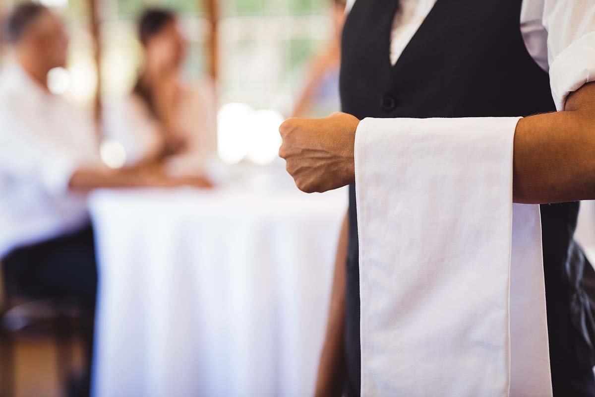 waiter standing in restaurant with white towel draped over arm