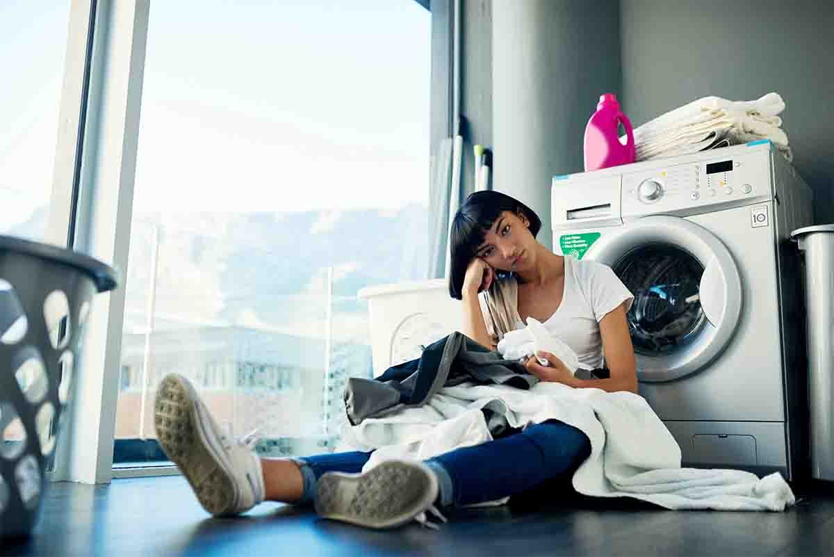 woman waiting for laundry cycle to finish in washing machine at home